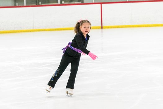 Little girl practicing figure skating moves on the indoor ice rink.