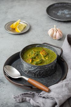 Traditional vegetarian Indian Punjabi food Palak Paneer with spinach and cheese in vintage metal bowl with spoon on rustic grey concrete background table, angle view