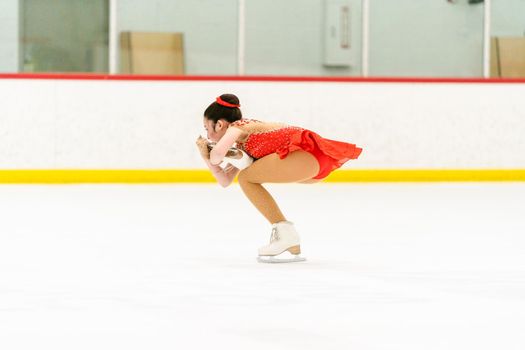 Teenage girl practicing figure skating on an indoor ice skating rink.