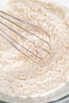 Mixing dry ingredients with a hand whisk in a large glass mixing bowl to bake lemon cupcakes.