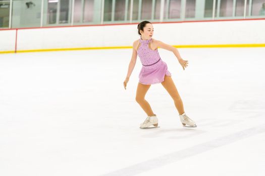 Teenage girl practicing figure skating on an indoor ice skating rink.