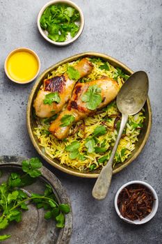 Biryani chicken, traditional dish of Indian cuisine, with basmati rice, fried onion, fresh cilantro in bowl on gray rustic stone background. Authentic Indian meal, top view, close-up