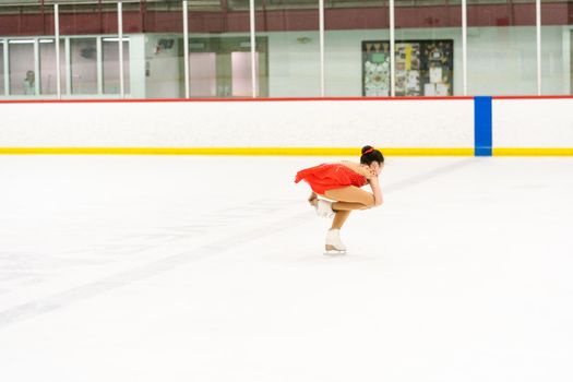 Teenage girl practicing figure skating on an indoor ice skating rink.