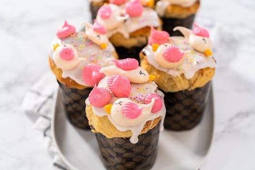 Freshly baked mini Easter bread kulich with lemon glaze, decorated with sprinkles and meringue bird-shaped cookies.