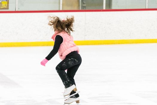 Little girl practicing figure skating moves on the indoor ice rink.