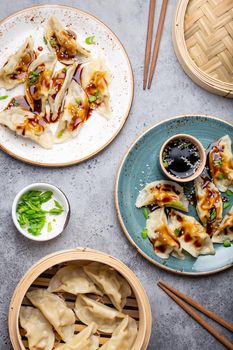 Close-up, top view of two plates with traditional Asian dumplings with soy sauce and chopsticks on gray rustic stone background. Authentic Chinese cuisine