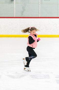 Little girl practicing figure skating moves on the indoor ice rink.