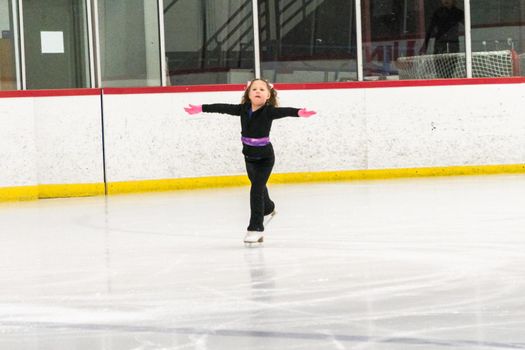 Little girl practicing figure skating moves on the indoor ice rink.