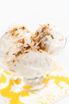 Homemade coconut ice cream garnished with roasted coconut flakes in a glass ice cream bowl.