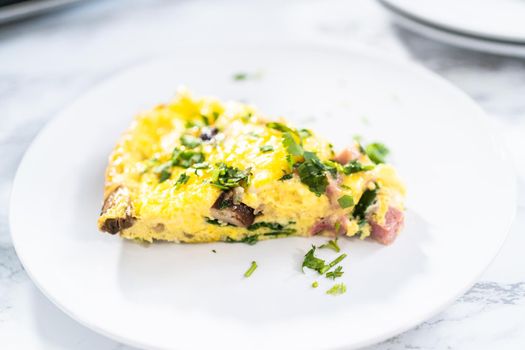 Slice of spinach and ham frittata on a white dinner plate.