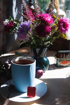 Blue cup of tea with bouquet of blue, pink and purple aster flowers in th bright light, morning tea concept, selective focus.