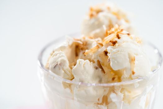 Homemade coconut ice cream garnished with roasted coconut flakes in a glass ice cream bowl.