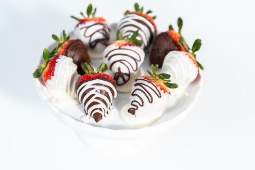 White and dark chocolate dipped strawberries on a white cake stand.