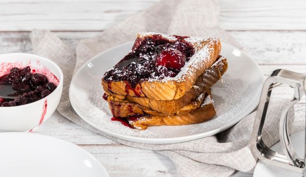 Stack of freshly made french toast garnished with mix berry compote and powder sugar.