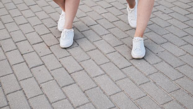 Two friends in white sneakers walk down the street