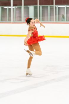 Teenage girl practicing figure skating on an indoor ice skating rink.