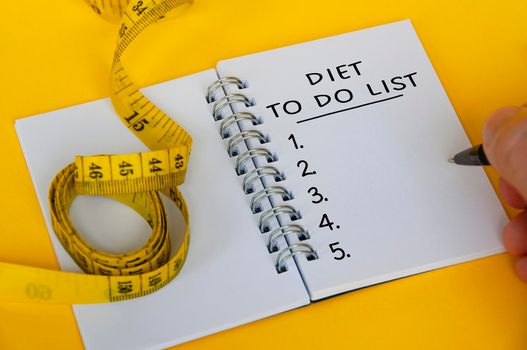 Diet to do list text on white notepad with measuring tape on yellow background. Health and diet concept.