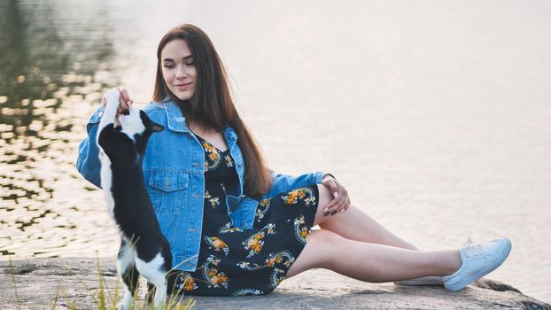 A girl plays with a cat by the lake