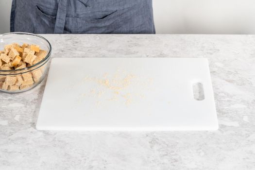 Cutting stale bread with a bread knife on a white cutting board to make croutons.