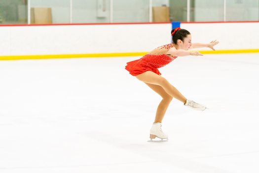 Teenage girl practicing figure skating on an indoor ice skating rink.