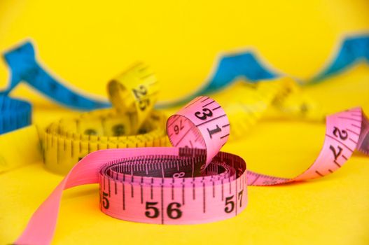 Red, yellow and blue measuring tapes on yellow cover background. Copy space and weight loss concept.