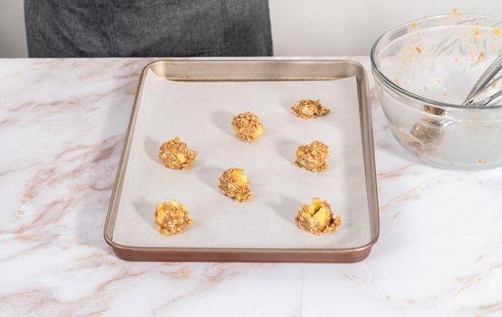 Scooping cookie dough into the baking sheet lined with parchment paper to bake apple oatmeal cookies.