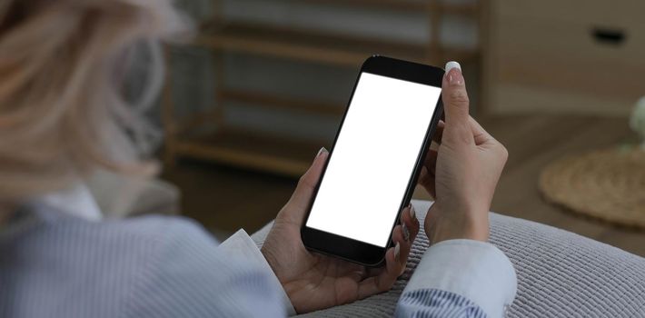 close-up image, Beautiful young Asian female using her smartphone while relaxing in her minimal living room. a woman holding a mobile phone white screen mockup..