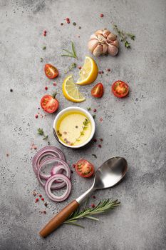 Food cooking ingredients arranged on grey stone rustic table with healthy vegetables, herbs, spices, olive oil and kitchen spoon from above