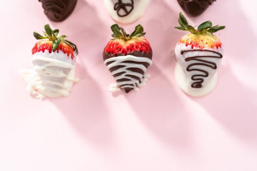 White and dark chocolate dipped strawberries on a pink background.