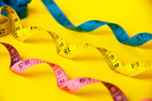 Red, yellow and blue measuring tapes on yellow cover background. Copy space and weight loss concept.
