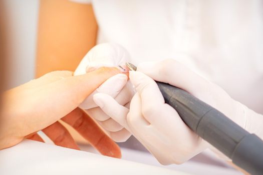 Closeup of manicure master in white gloves applying an electric nail file drill to remove the nail polish in the beauty salon