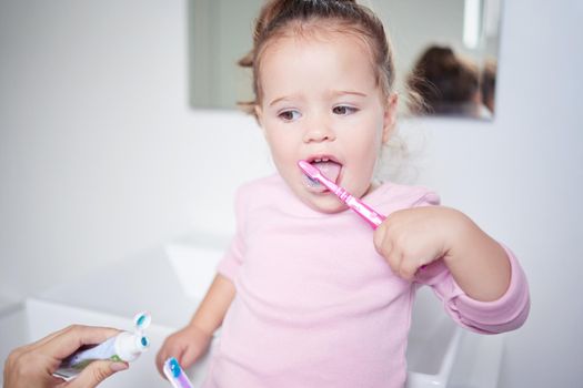 Baby learning to brush her teeth, dental and oral hygiene. Toothbrush, toothpaste and brushing teeth in child development and routine. Dentist, dentistry and teeth cleaning in young children