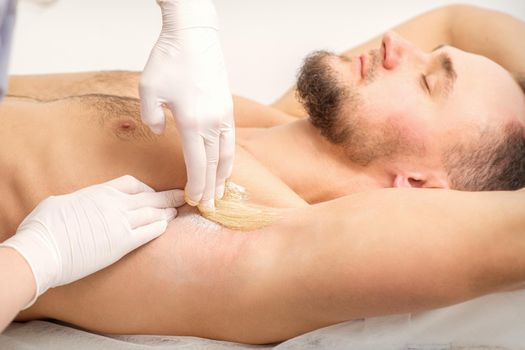 Young caucasian man receiving hair removal from his armpit in a beauty salon, depilation men's underarm