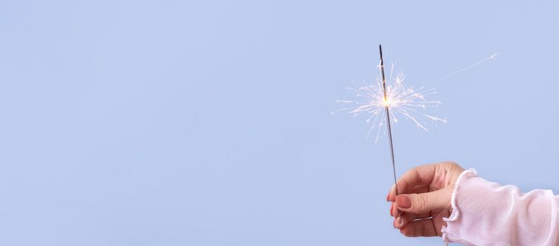 sparklers in a woman's hand on a blue background with copy space. Christmas holiday concept.