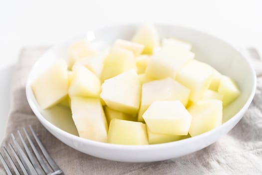 Sliced golden dewlicious melon in a white bowl.