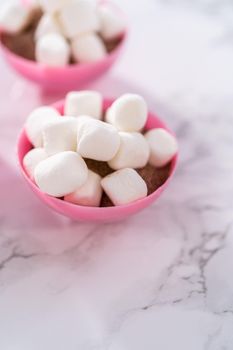 Filling in pink chocolate shells with hot chocolate mix and mini marshmallows to prepare hot chocolate bombs.