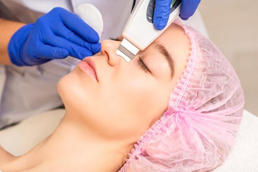 Closeup of beautiful young woman receiving ultrasound facial exfoliation and cavitation facial peeling with ultrasonic equipment in cosmetology office