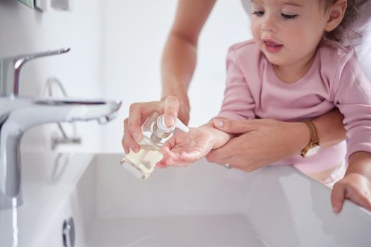 Mother cleaning kids hands with sanitizer liquid soap after baby toddler had dirty fingers in the sink. Healthy, grooming and mom cleaning and helping a young girl with hygiene wellness at home.