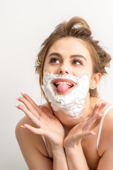 Portrait of a beautiful young smiling caucasian woman posing with shaving foam on the face stuck out her tongue on white background