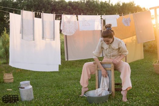 Laundry day. A woman hangs linen and towels on a tree in the courtyard of a village house. Summer cottage concept.