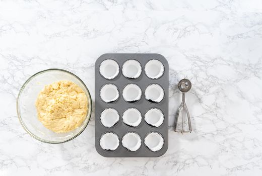 Flat lay. Scooping cupcake dough with a dough scoop into foil liners to bake lemon cupcakes.