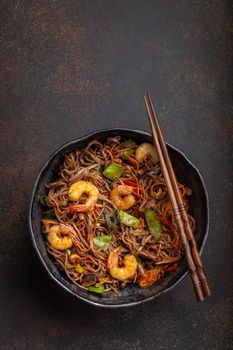 Close-up of Chinese soba stir-fry noodles with shrimps, vegetables in rustic ceramic bowl pan served on concrete background, close up, top view. Traditional asian/thai dish, Chinese style meal