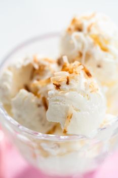 Homemade coconut ice cream garnished with roasted coconut flakes in a glass ice cream bowl.