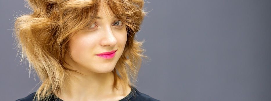 Beautiful young caucasian woman with a red short curly hairstyle on dark background