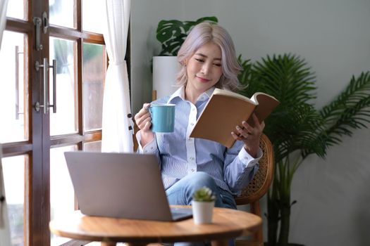 Portrait Asian woman reading book and relaxing with coffee at home.