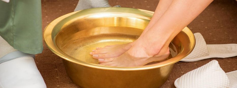 Female feet in a golden bowl with water in spa salon. Spa treatment