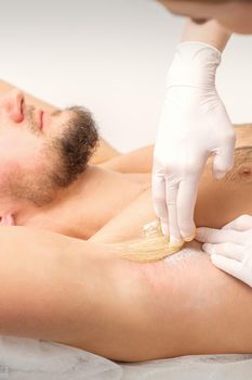 Young caucasian man receiving hair removal from his armpit in a beauty salon, depilation men's underarm