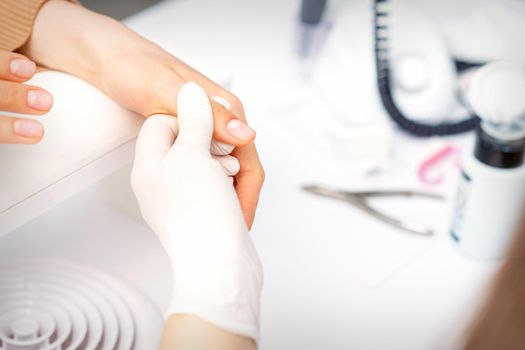 The manicurist holds the female thumb during a manicure procedure in the nail salon