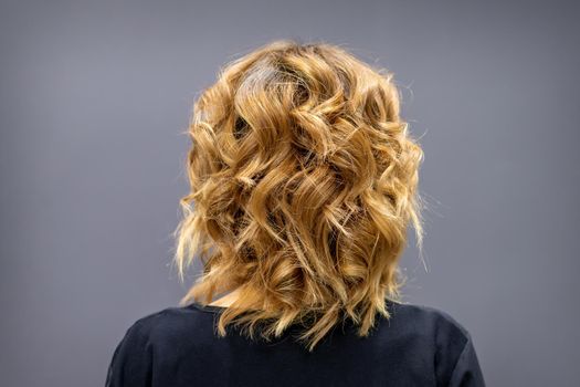 Back view of the woman with long brown curly hair stands on a dark background