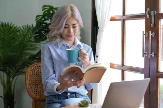 Asian woman reading a book and drinking coffee in the morning..